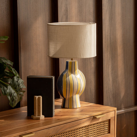 Striped ceramic lamp styled on a wooden dresser next to a small plant.