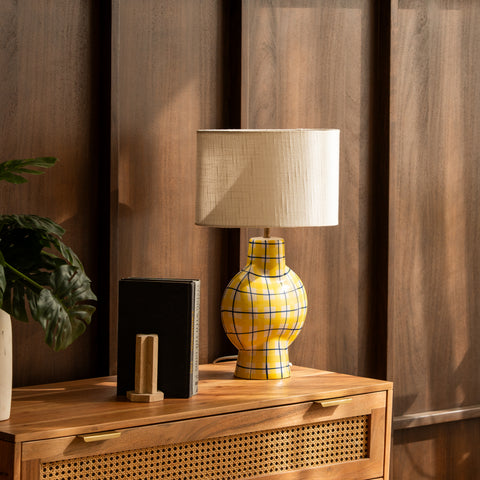 Plaid ceramic table lamp styled on a wooden dresser against wood walls.