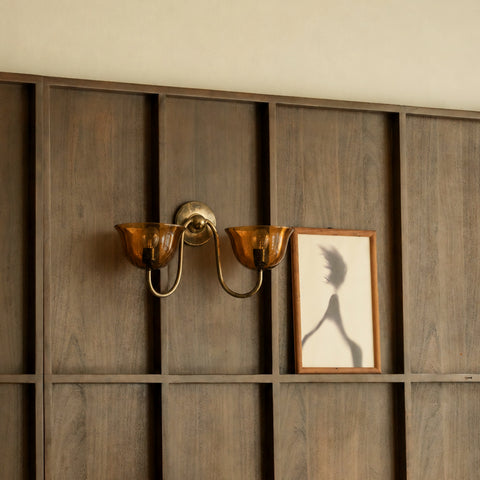 Brass wall sconce mounted on a dark wood paneled wall next to framed art