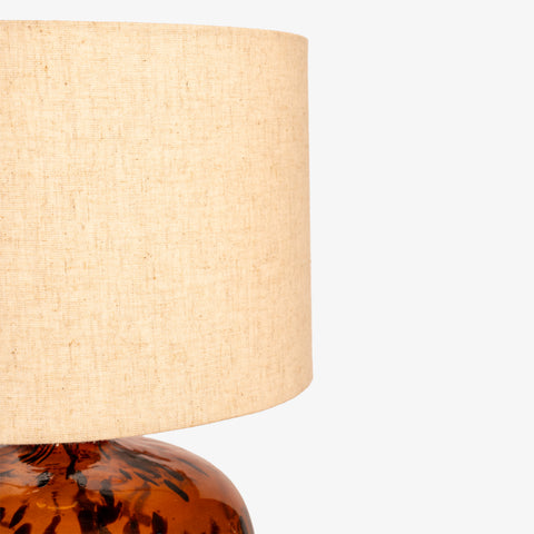 Close-up crop of the textured tan fabric lampshade and glass base.