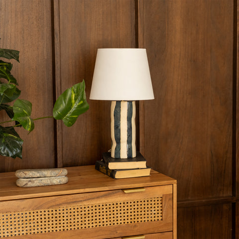 Small table lamp styled on a wooden dresser next to books and a plant.