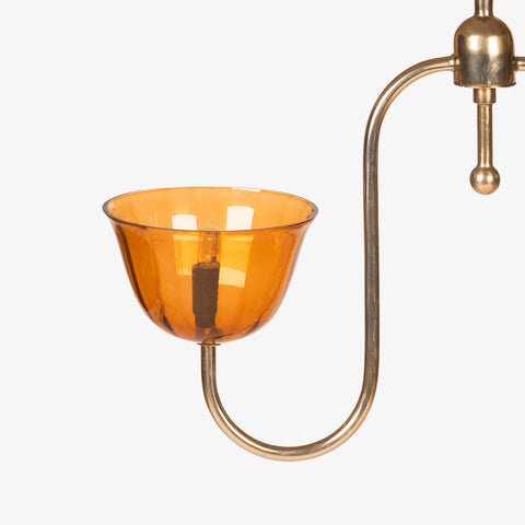 Close-up of a single curved brass arm and its amber glass cup shade.