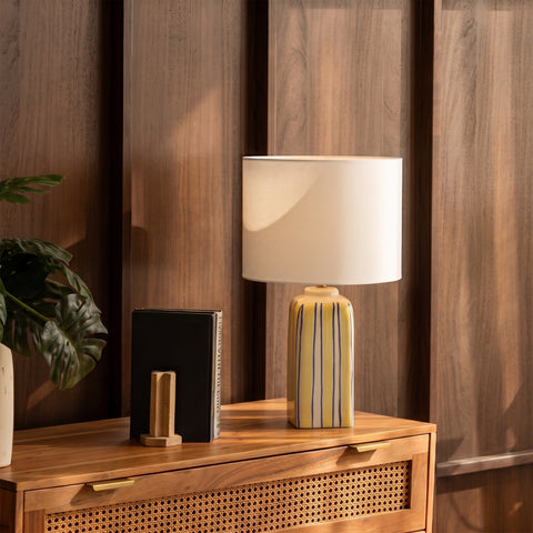 Striped ceramic lamp styled on a wooden dresser next to a small plant.