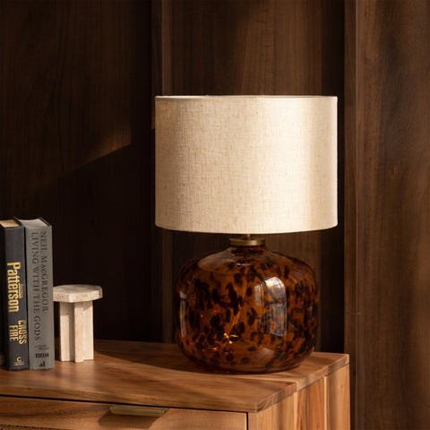 Tortoiseshell glass lamp styled on a wooden tabletop next to books.