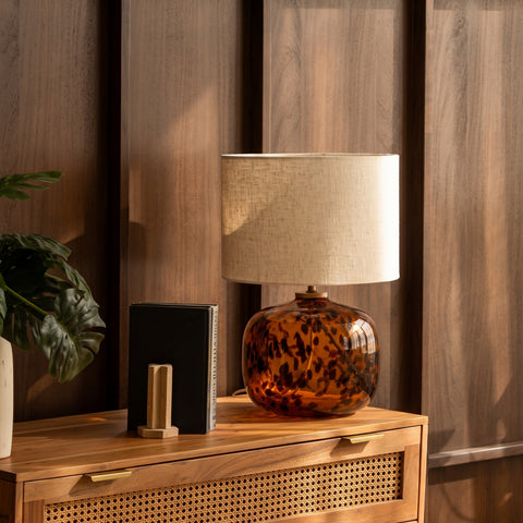 Tortoiseshell table lamp styled on a modern wooden credenza against wood walls.