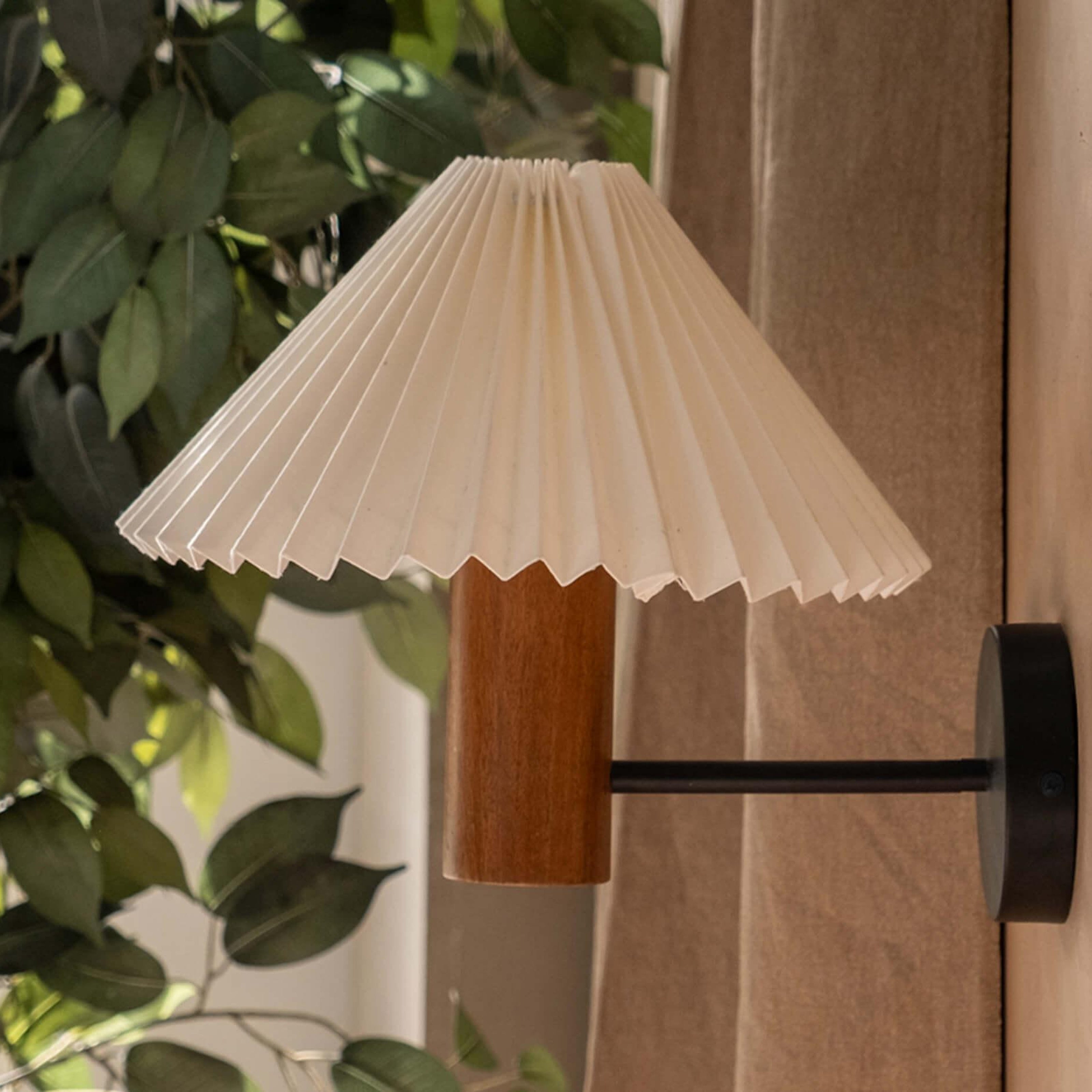 White pleated shade wall lamp with a natural wooden cylindrical base in walnut finish, perfect as a bedside wall lamp or decorative wall sconce for minimalist and vintage interiors.