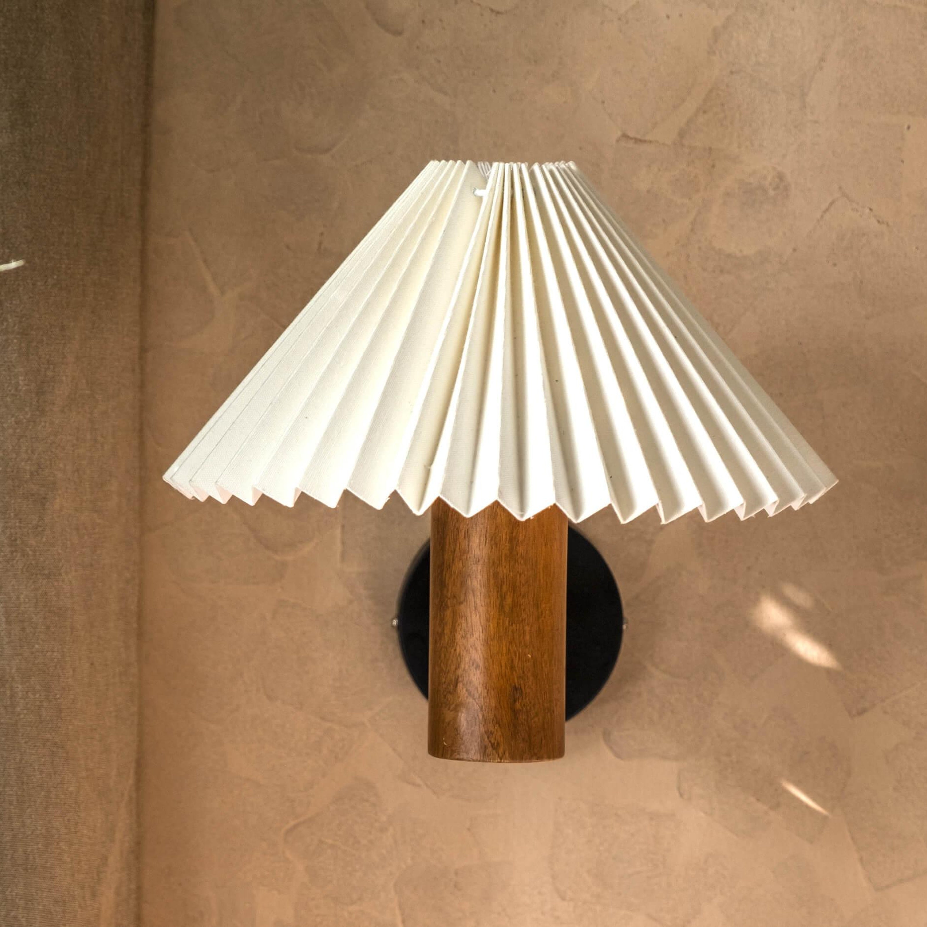 White pleated shade wall lamp with a natural wooden cylindrical base in walnut finish, perfect as a bedside wall lamp or decorative wall sconce for minimalist and vintage interiors.