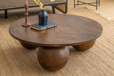 Wooden coffee table with spherical bases on a carpeted floor