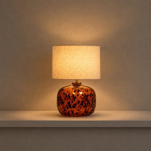 Illuminated tortoiseshell table lamp casting a warm glow in a dark setting.