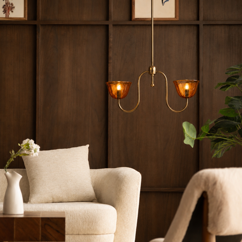 Brass pendant light hanging in a modern living room with dark wood paneling.