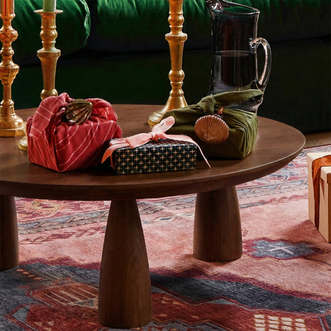Round wooden coffee table with festive decor, brass candle holders, and fabric-wrapped gift accents in living room 