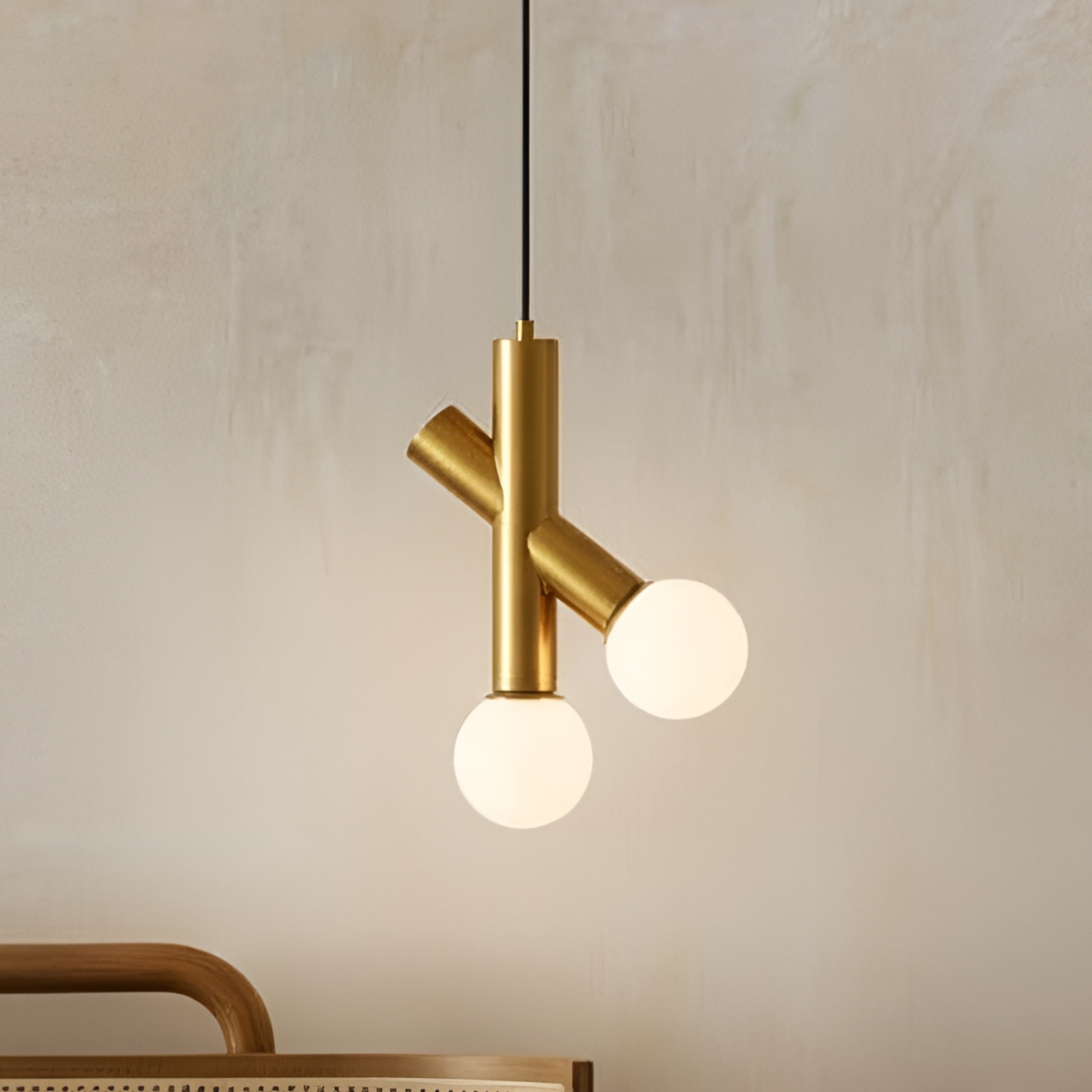 Modern hanging lights for living room featuring a gold pendant lamp with two frosted globe bulbs set against a textured neutral wall.