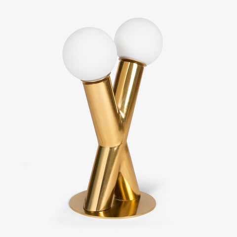 A front-facing studio shot of the gold table lamp featuring two interlocking cylindrical pillars topped with white frosted glass globes.