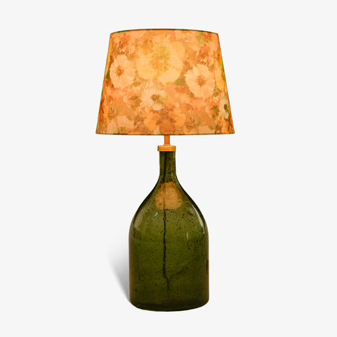 Studio shot of the glass bottle lamp with its floral shade lit up.