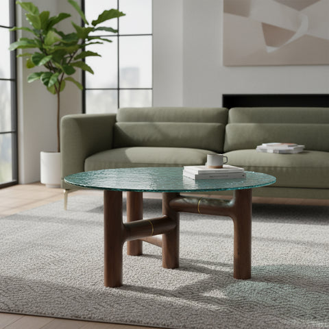 A round coffee table with a textured green glass top and dark wood tripod base in a living room.