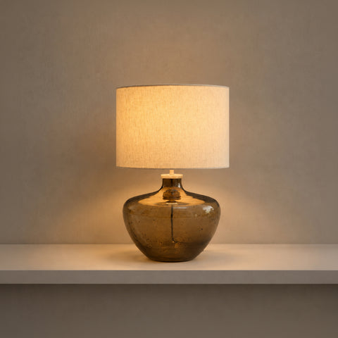 Illuminated smoky glass table lamp glowing warmly in a dim room.
