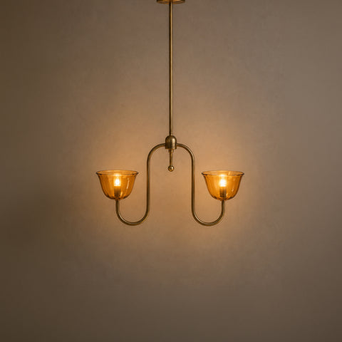 Illuminated double-arm brass pendant chandelier glowing warmly in a dim room.