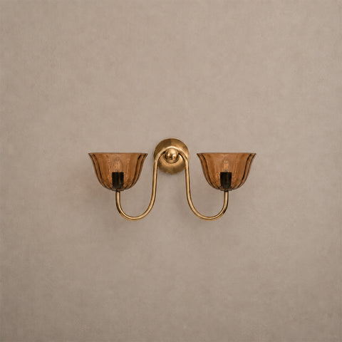 Double-arm brass wall sconce with amber glass shades on a plain background.