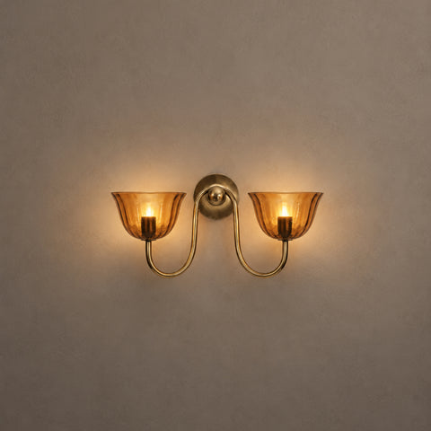 Illuminated brass double wall sconce glowing warmly in a dim setting.