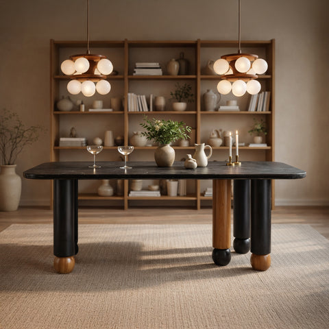 A dark marble-top dining table featuring thick, mismatched cylindrical legs in black and wood finishes with spherical feet.