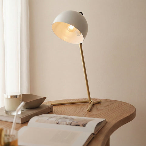 Modern white and brass desk lamp on a round wooden table with an open book.