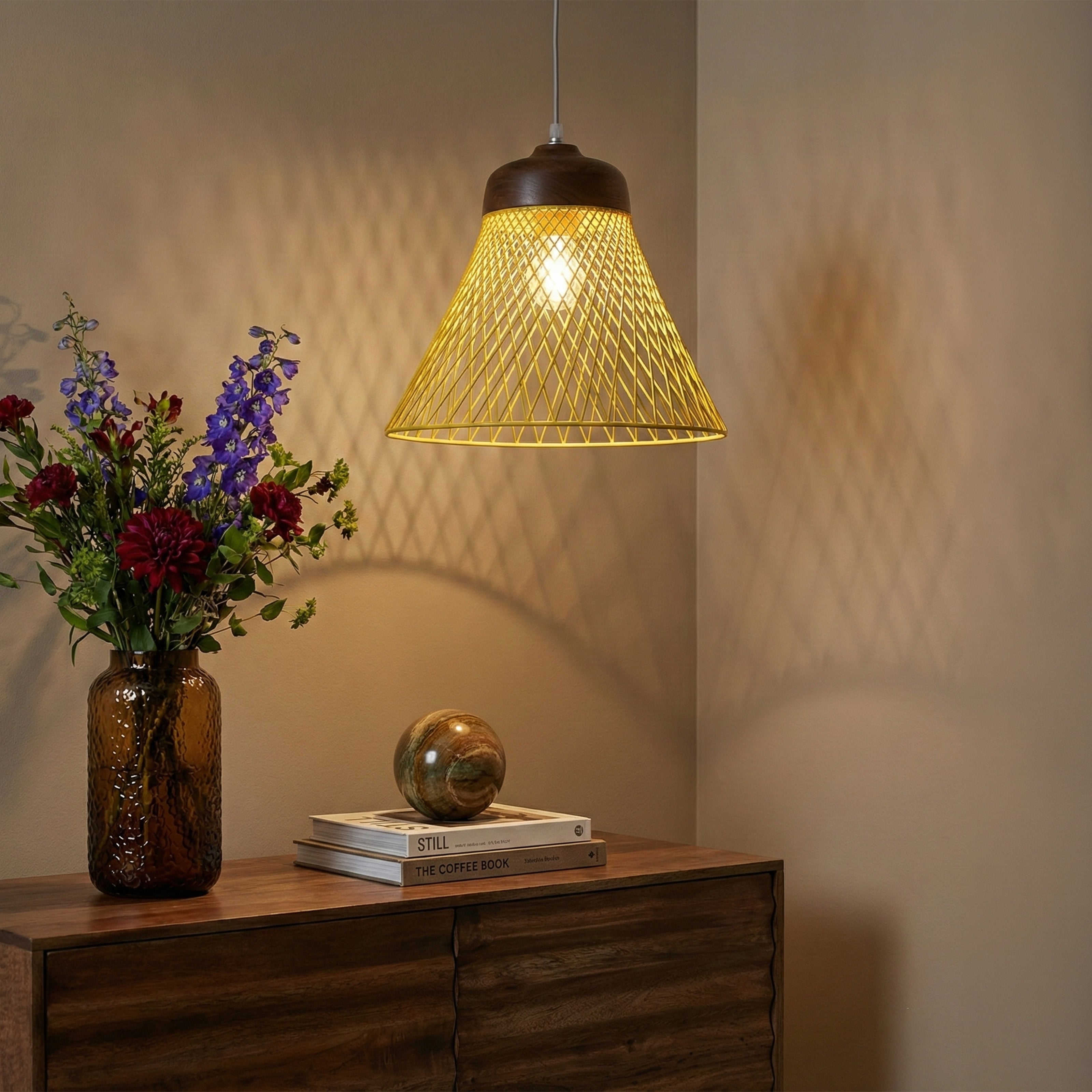 Yellow wire pendant light hanging above a wooden sideboard with flowers and books.
