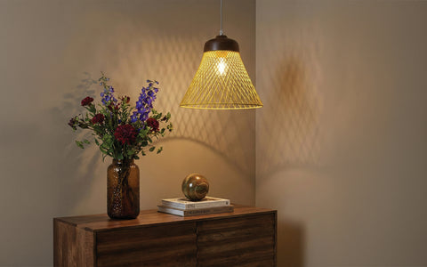 Yellow wire pendant light hanging above a wooden sideboard with flowers and books.