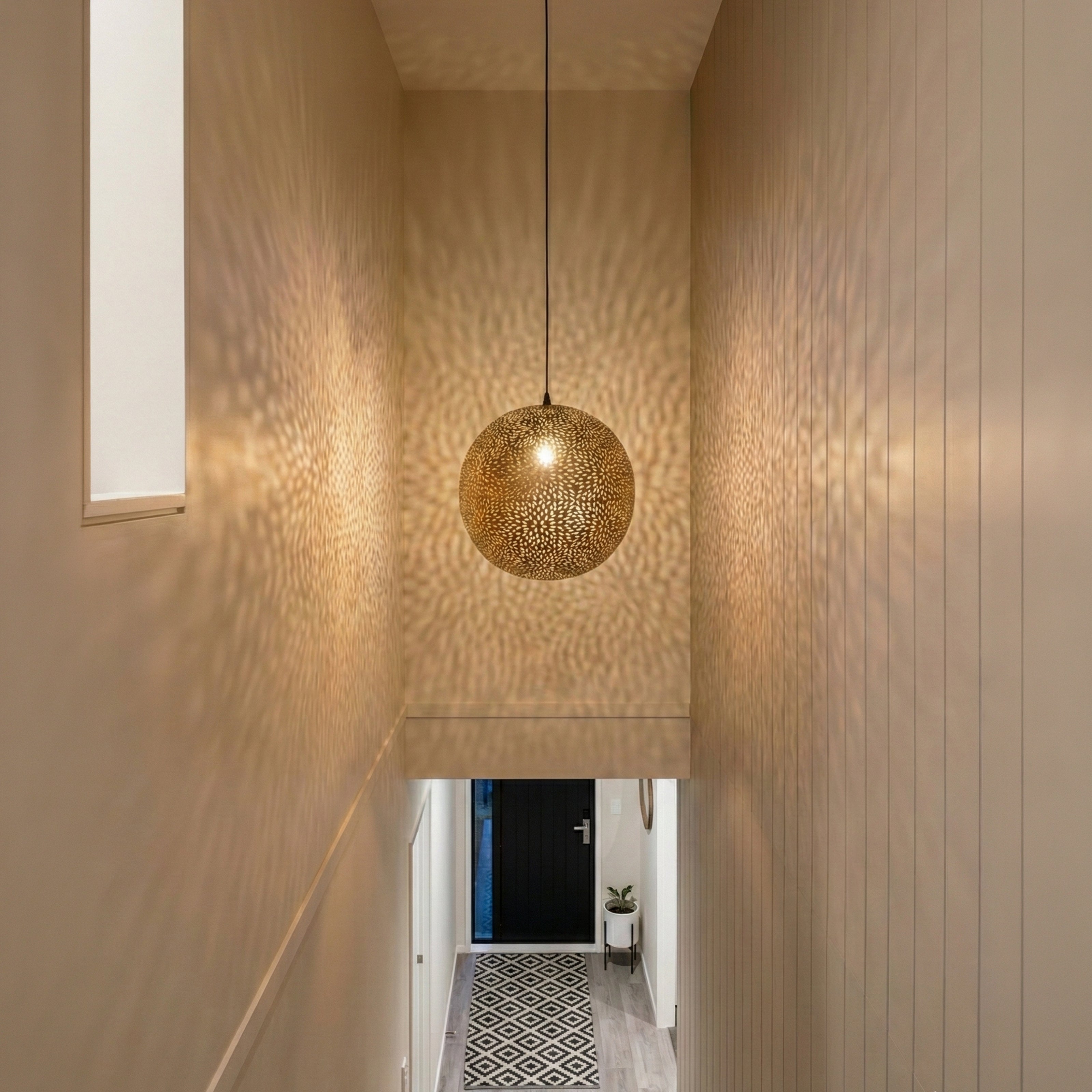 A patterned spherical pendant light casting soft shadows in a tall hallway.