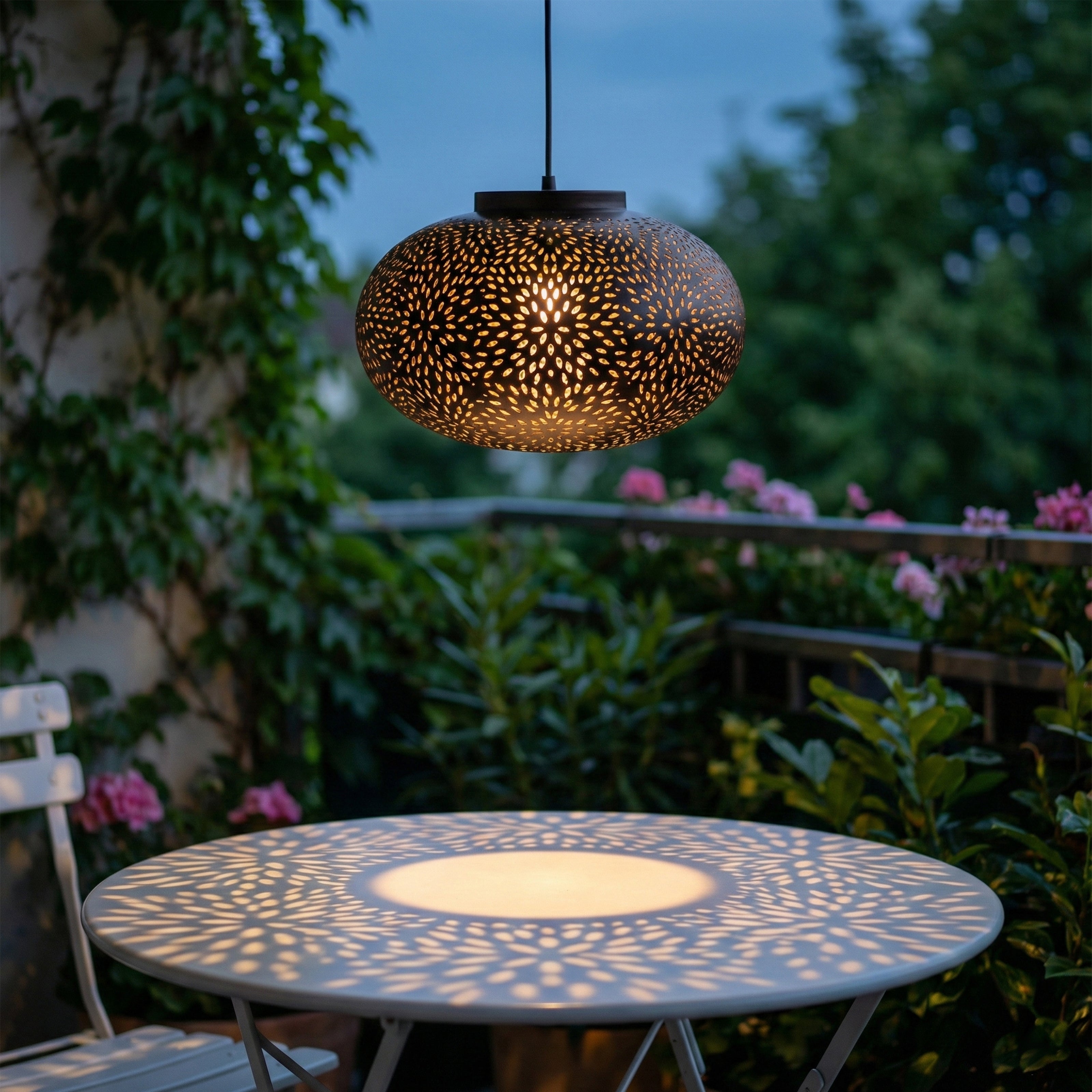 Perforated black pendant light casting patterned shadows over an outdoor table at dusk.