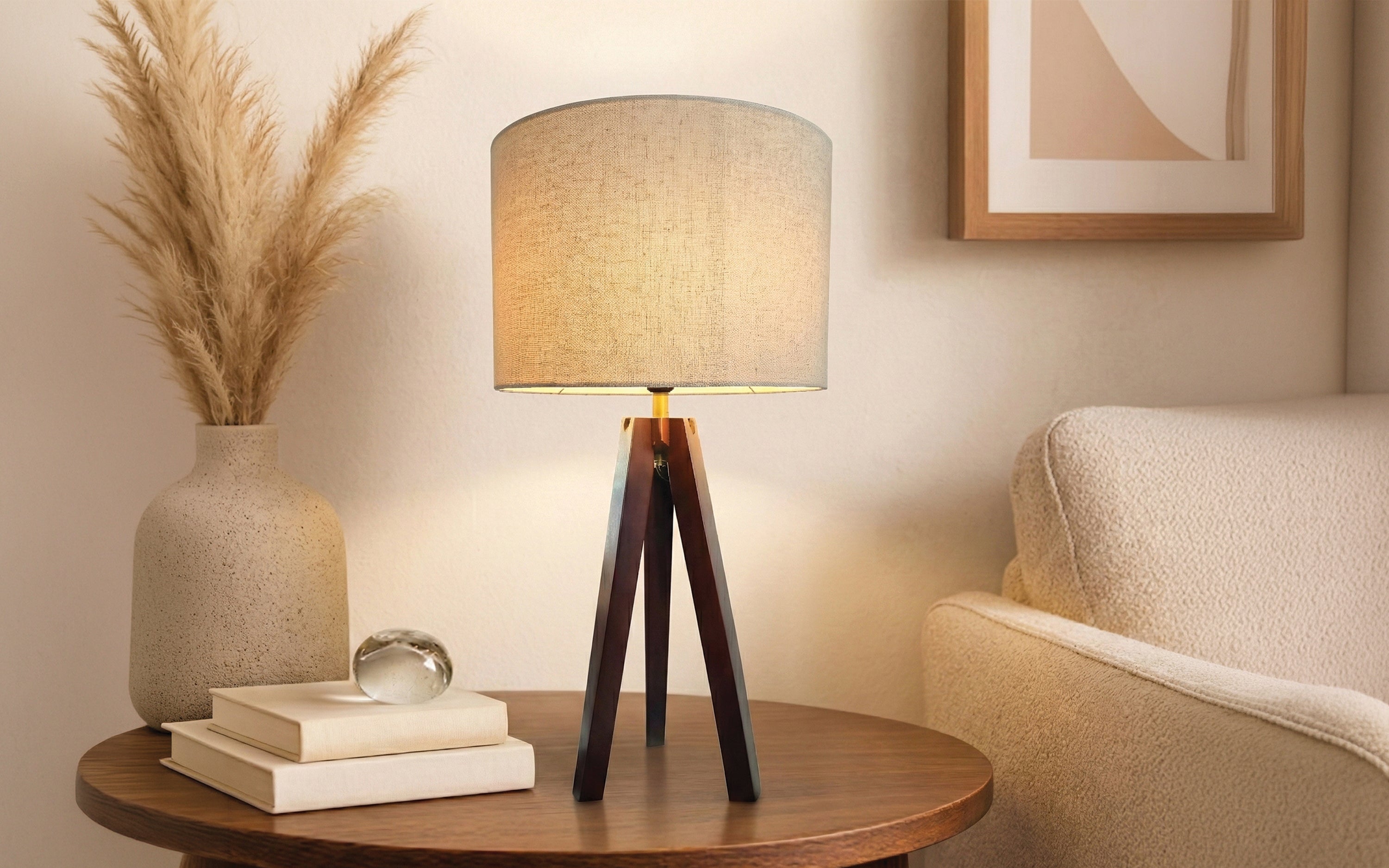 A warm table lamp with a fabric shade and tripod wood base on a round wooden table.