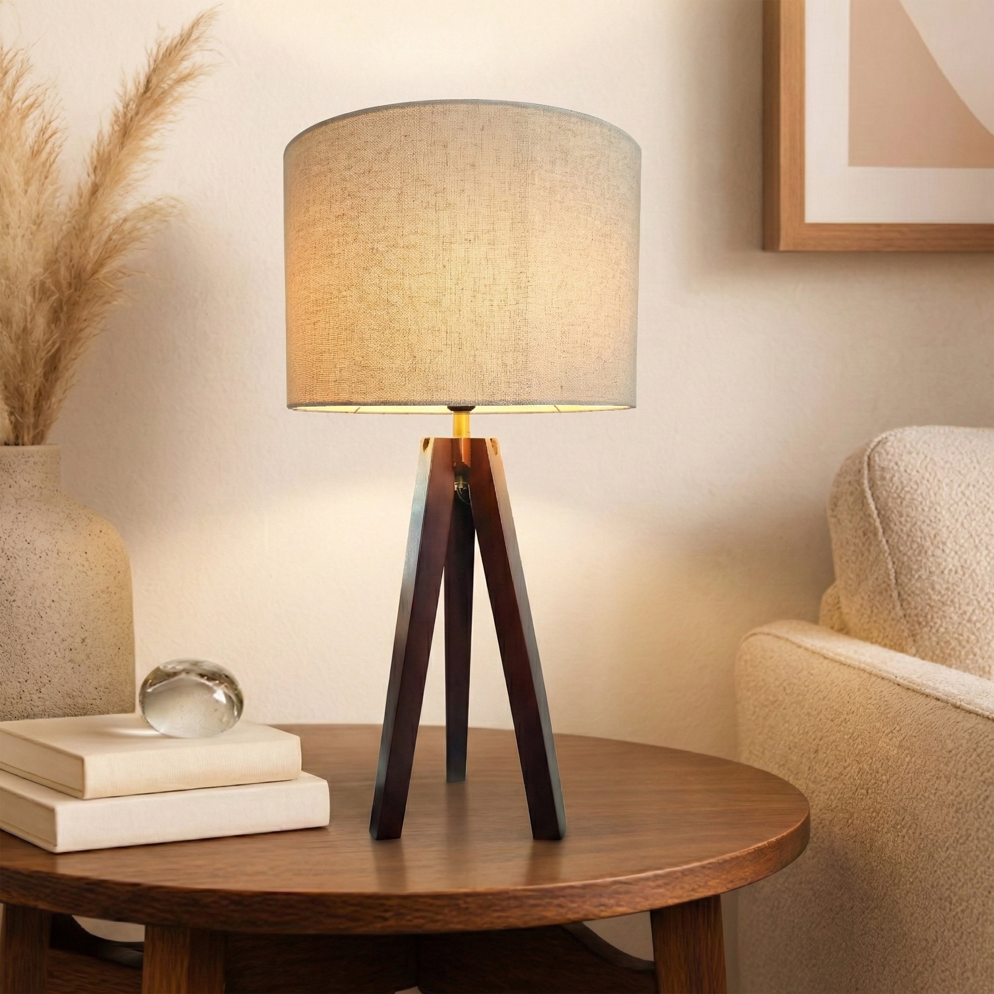 A warm table lamp with a fabric shade and tripod wood base on a round wooden table.