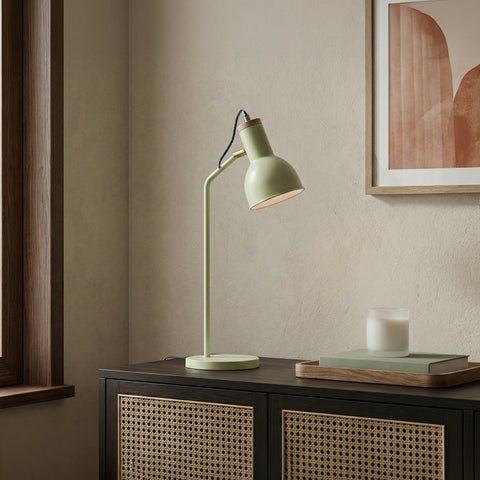 A sage green industrial-style desk lamp with a wood accent sitting on a dark wood cabinet.