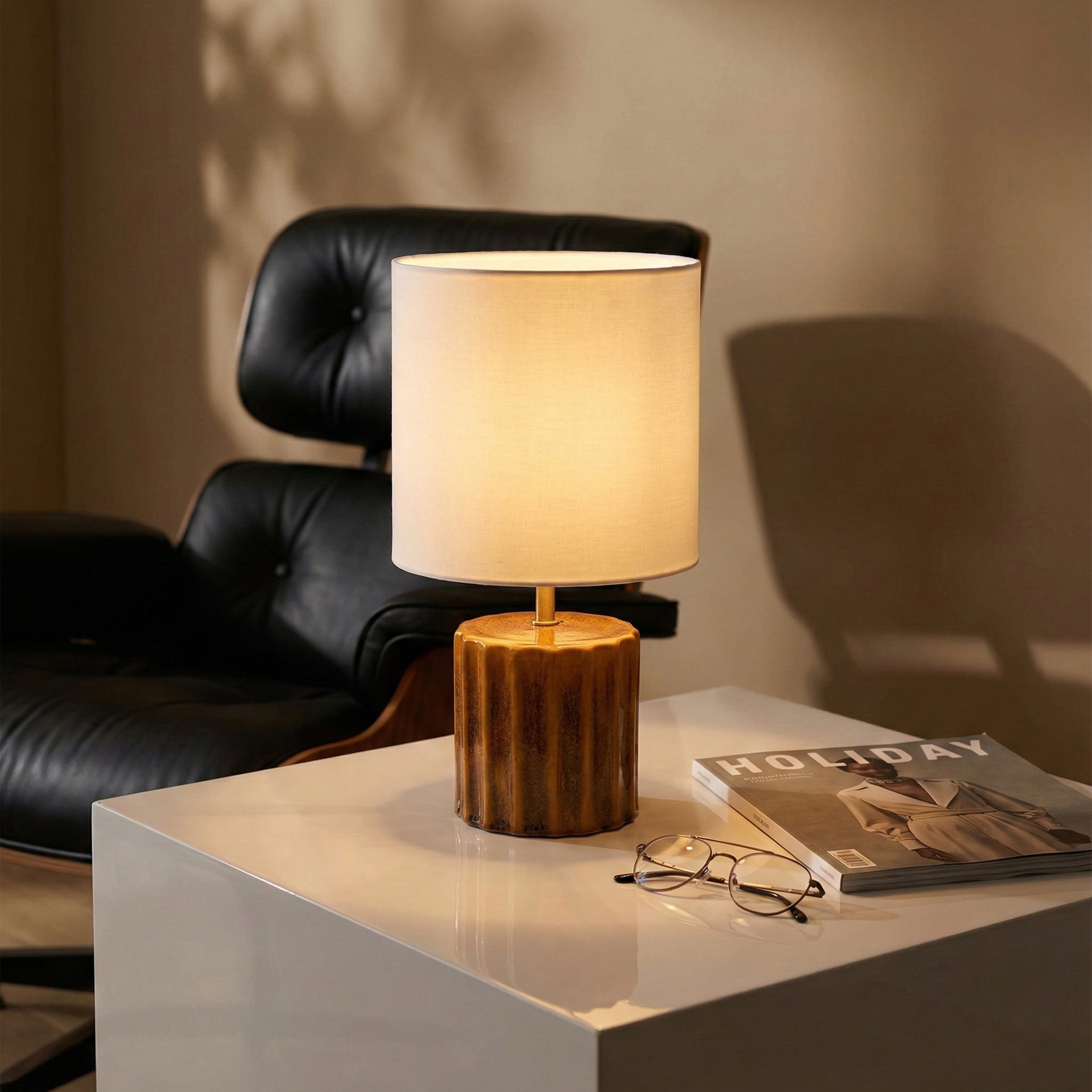Ceramic table lamp with a ribbed amber base and white drum shade.