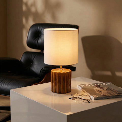 Ceramic table lamp with a ribbed amber base and white drum shade.