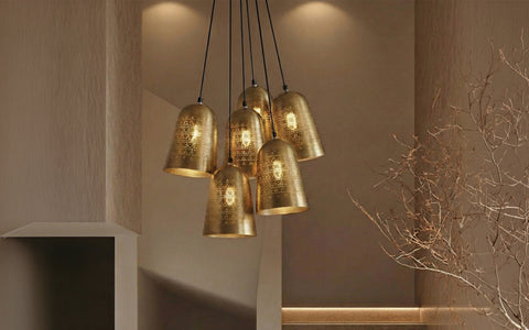 A multi-light cluster pendant featuring seven perforated brass bell shades suspended over a staircase.