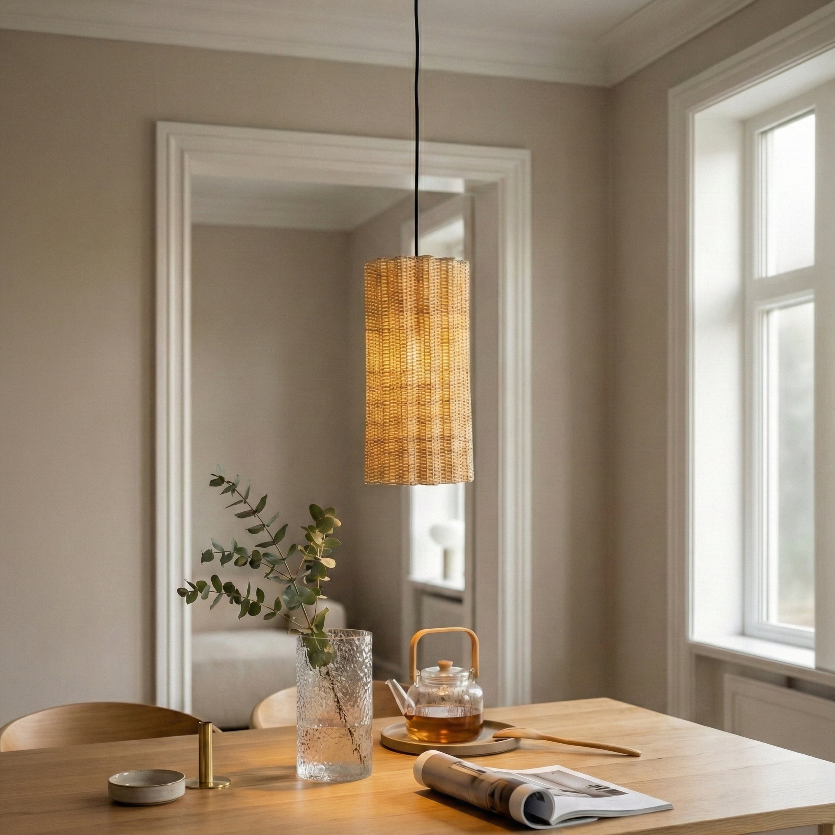 A cylindrical, woven rattan pendant light hangs over a wooden dining table