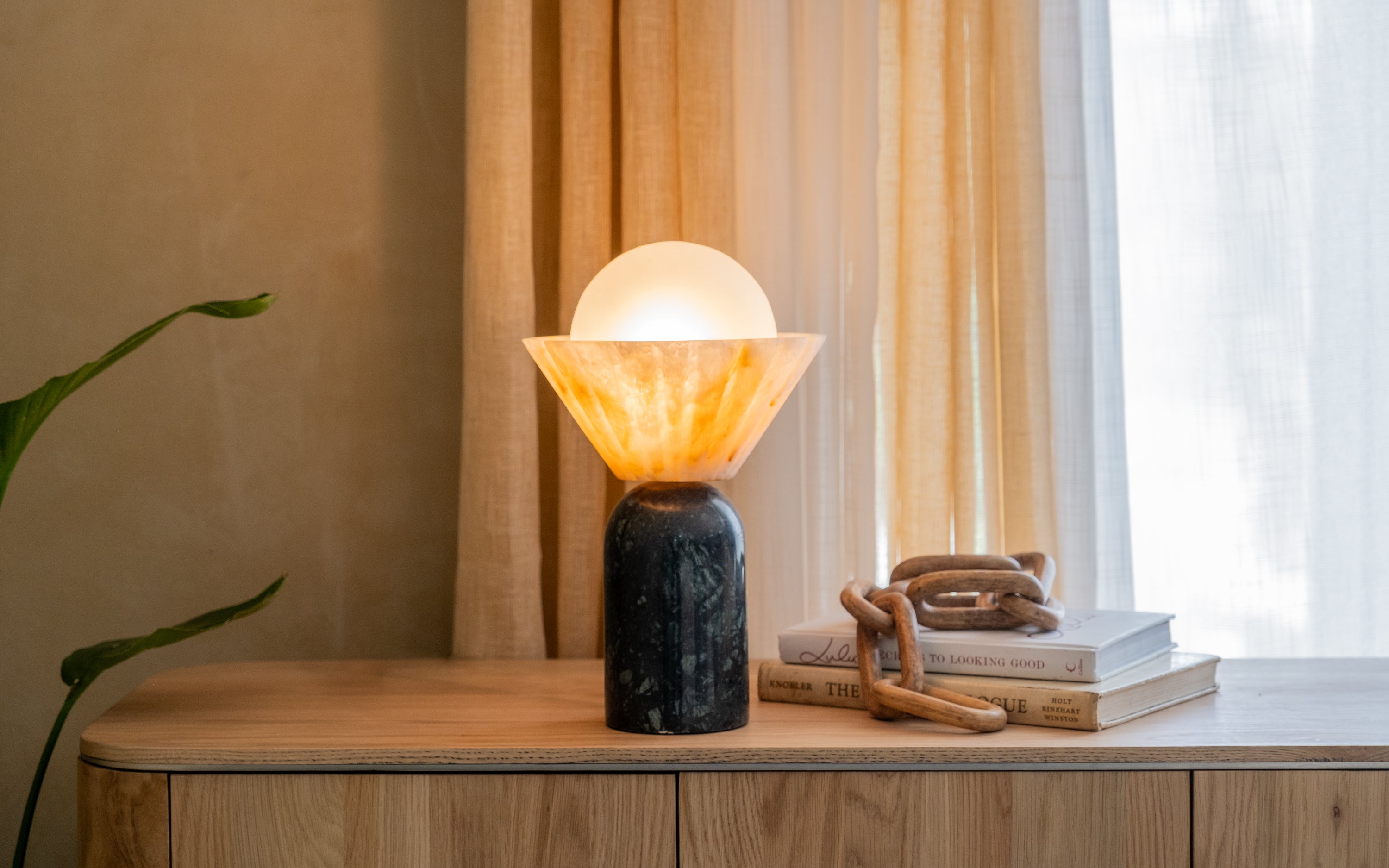 Stylish marble table lamp with glowing orb and amber-toned shade, placed on a console with books and decor accents.