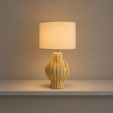 Illuminated striped table lamp glowing warmly on a shelf in a dim room.