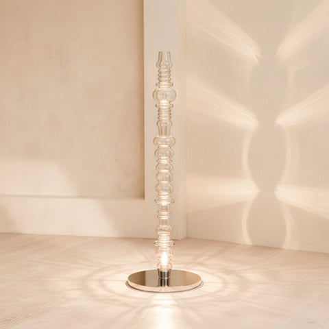 Reef glass floor lamp placed in corner with warm light pattern on wall, modern interior lighting.