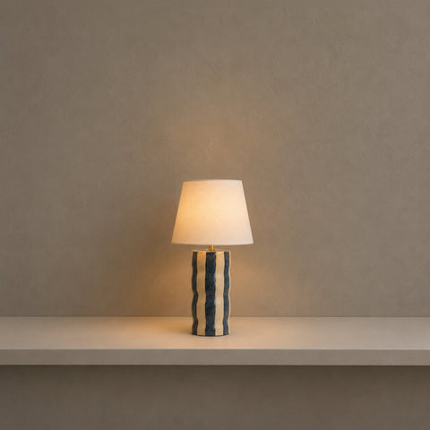 Small patterned table lamp illuminated with a warm glow in a dark room.