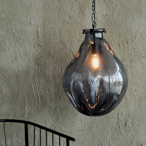 A black hanging lamp with a glass bulb and a steel frame, illuminated and hanging against a textured wall.