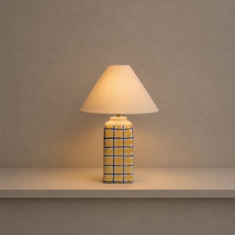 Illuminated striped table lamp glowing warmly on a shelf in a dim room.
