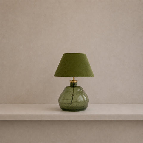 Small green glass table lamp with a matching green fabric shade on a shelf.