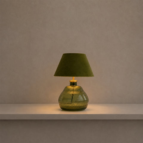 Small green glass lamp illuminated with a warm glow in a dim setting.