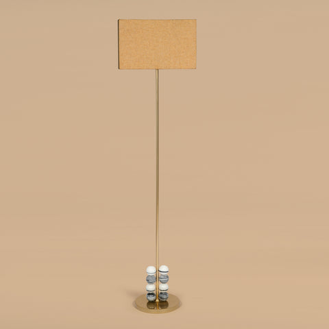 Contemporary floor lamp with fabric shade and brass stem in neutral interior setting.
