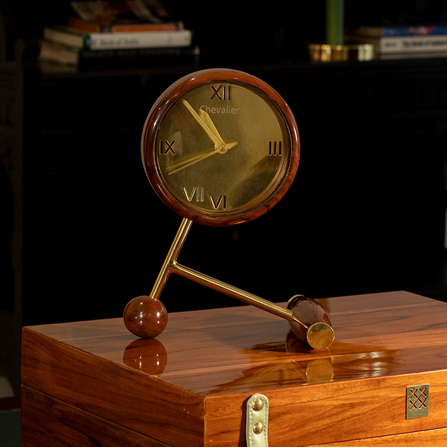 Desk clock with a gold face and wooden rim on a tripod stand against a dark background.