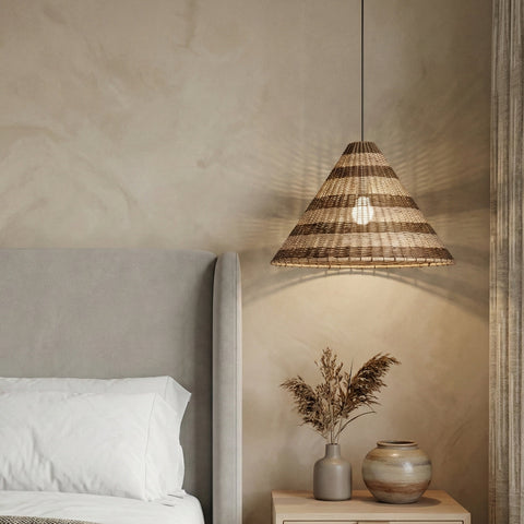 Woven pendant lamp hanging beside a bed in a calm, neutral bedroom.