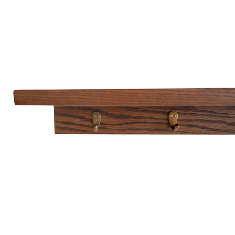 Angled view of Kanso wooden wall shelf showing the raised ledge and brass hooks below